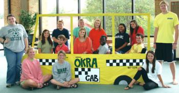 students posing with a cardboard 'okra cab' cutout