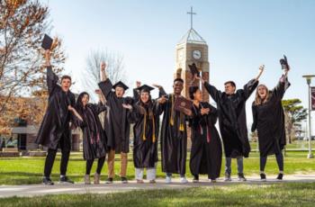 graduates cheering with diplomas in front of a clock tower