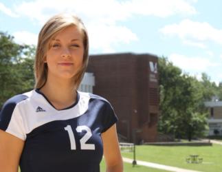 female athlete in volleyball jersey number 12 with campus building behind