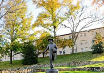 statue of a person with autumn trees and a building behind