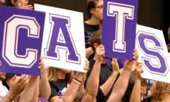 crowd holding signs spelling 'CATS' at an event