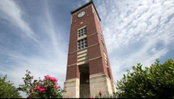 brick clock tower with flowers and a cloudy sky