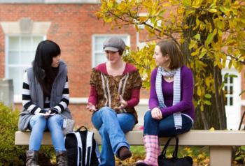 three students sitting on a bench talking