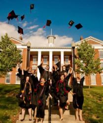 graduates tossing caps in front of a brick building