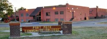 brick building behind 'fort peck community college' sign at dusk