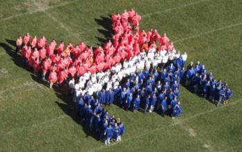 students in colored outfits form a '25' on a grass field