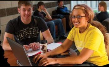 two students smiling at a laptop in a campus setting