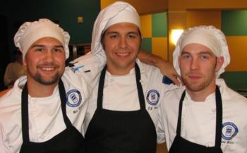 three smiling chefs in white hats and aprons