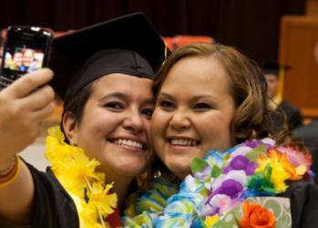 graduates taking a selfie, adorned with leis and smiles