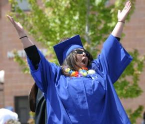 graduate in blue gown and cap cheering with arms raised