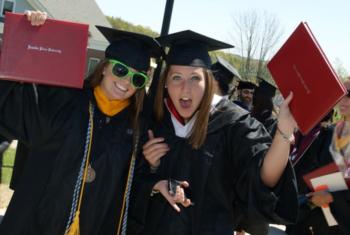 two graduates posing with diplomas