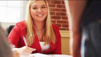 smiling woman in red top sitting at a table with pen