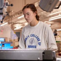 student operating machinery with college logo