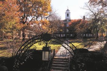 wrought iron gate displaying university emblem in foreground, building in fall setting