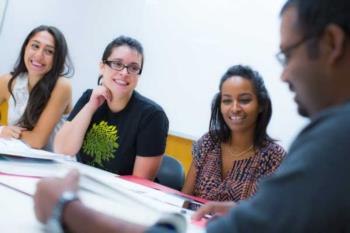 three students smiling at a table with a teacher, in a classroom