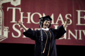 graduate celebrating on stage with 'thomas edison state university' banner