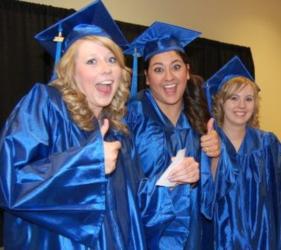 three graduates in blue gowns giving thumbs up