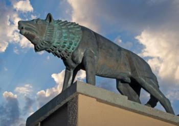 bronze statue of a wolf against a cloudy sky