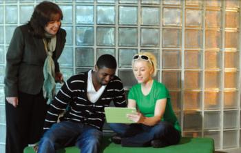 three students discussing over a tablet near glass blocks