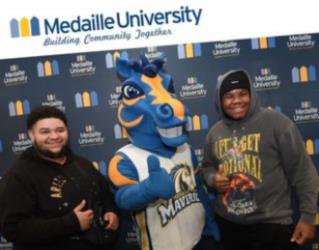 two people with a mascot, 'medaille university' backdrop