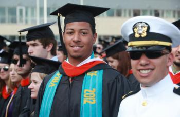 graduate in cap and gown with military personnel smiling