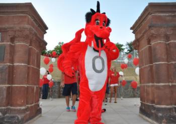 mascot in front of archway with red balloons