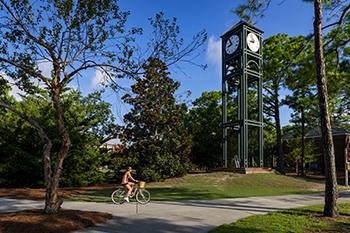 cyclist passing by tall clock tower on sunny day