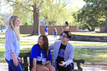 three students laughing on a bench outdoors