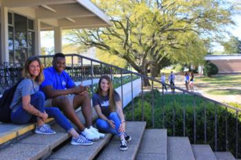 students sitting on steps with campus building behind