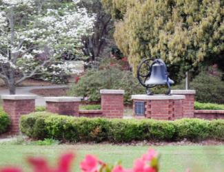 bell on brick pedestal in campus garden