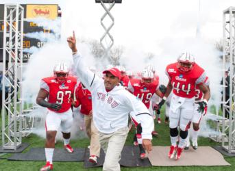 football team entering field with coach leading