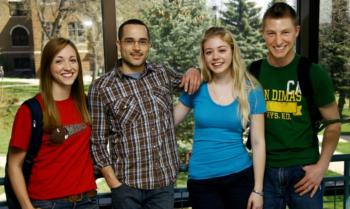 four students smiling in front of a campus view