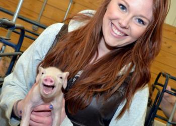 smiling woman holding a piglet in barn