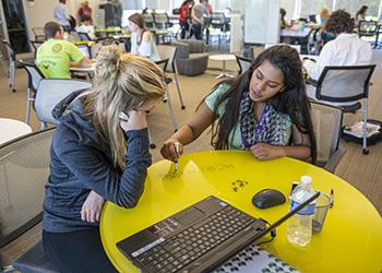 two students studying with a laptop on a yellow table