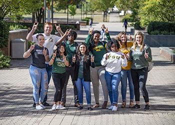 group of students giving thumbs up in front of campus