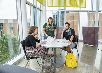 students discussing over a large blueprint at a table