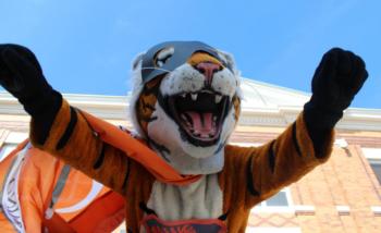 tiger mascot with arms up against a clear sky