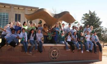 group of students sitting on a sculpture with university seal