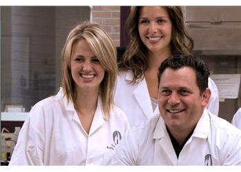 three smiling people in white lab coats