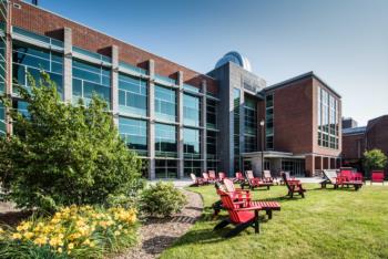 science building with red chairs &amp; blooming flowers