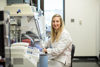 student working with lab equipment smiling at camera