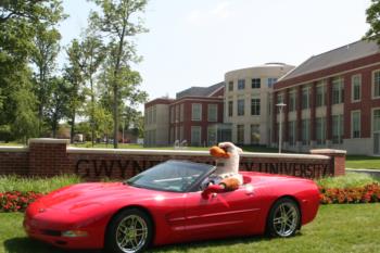 red sports car with mascot in front of sign