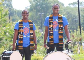 two people with drums wearing colorful scarves