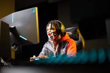 student at a gaming station wearing a mask