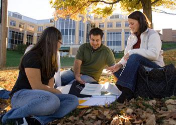 three students studying on campus lawn