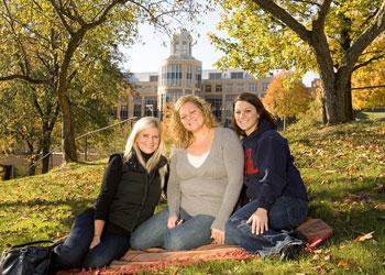 students sitting by campus building in fall