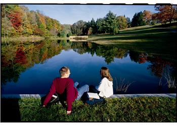 two people sitting by a pond with autumn trees