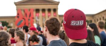 crowd facing building, person in 'sju' hat