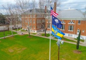 us and university flags in front of campus buildings