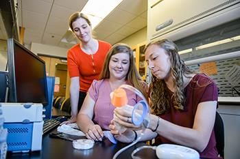 three women examining a breast pump in a lab setting